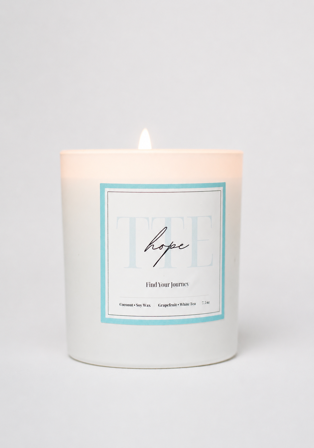 A white glass jar candle with a single lit wick, featuring a square label with a light blue border and the word 'hope' in script, set against a clean white background.